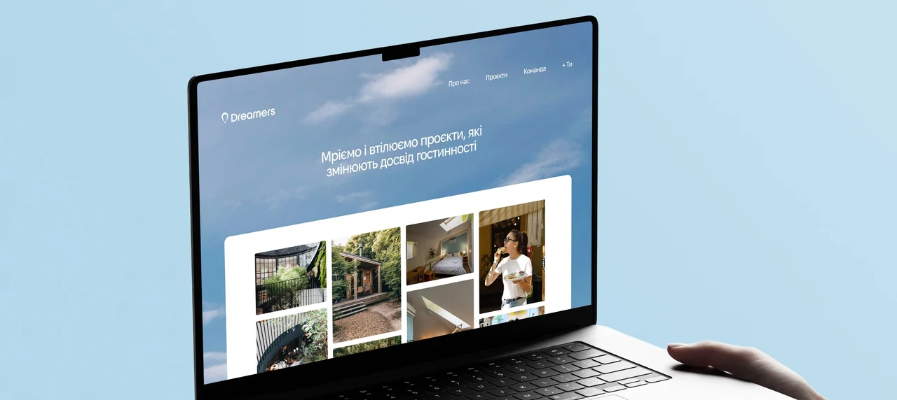 Dreamers website on a laptop, held against a pale blue sky